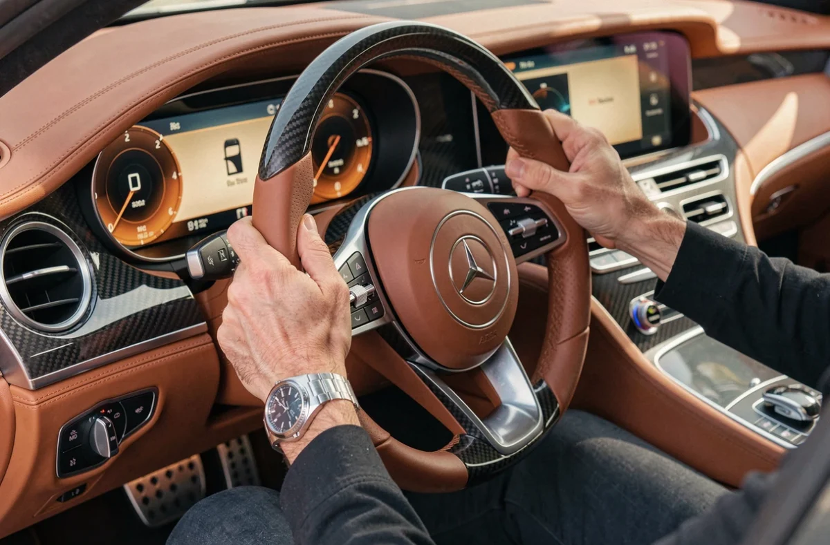 Intérieur luxueux d'une voiture de prestige avec siège en cuir cognac, volant carbone et montre mécanique au poignet du conducteur